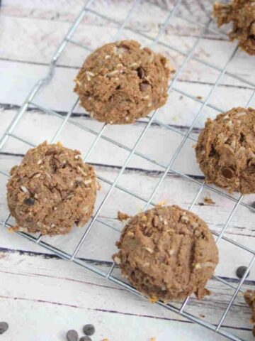 Chocolate vegan protein cookies on a cooling rack with ingredients around the rack