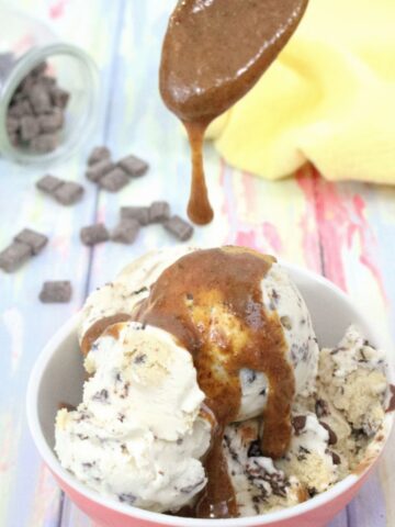 Caramel magic shell being drizzled onto dairy-free ice cream in a peach bowl with chocolate chips behind it.