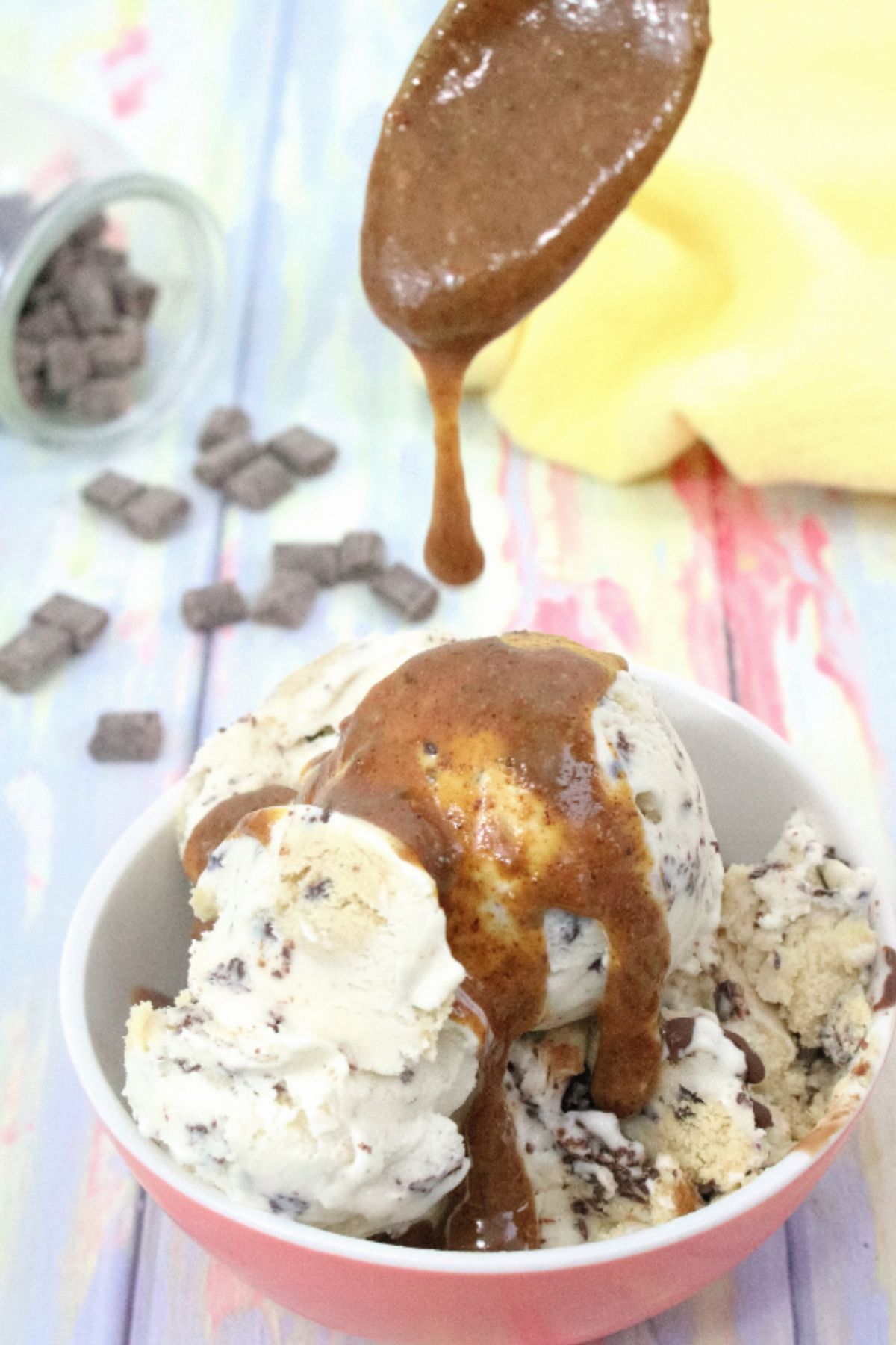 Caramel magic shell being drizzled onto dairy-free ice cream in a peach bowl with chocolate chips behind it.