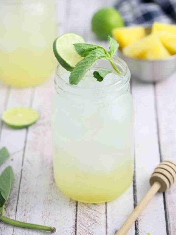 Ginger beer mocktail in a mason jar with fresh mint and lime on the jar and ingredients and another jar around it.