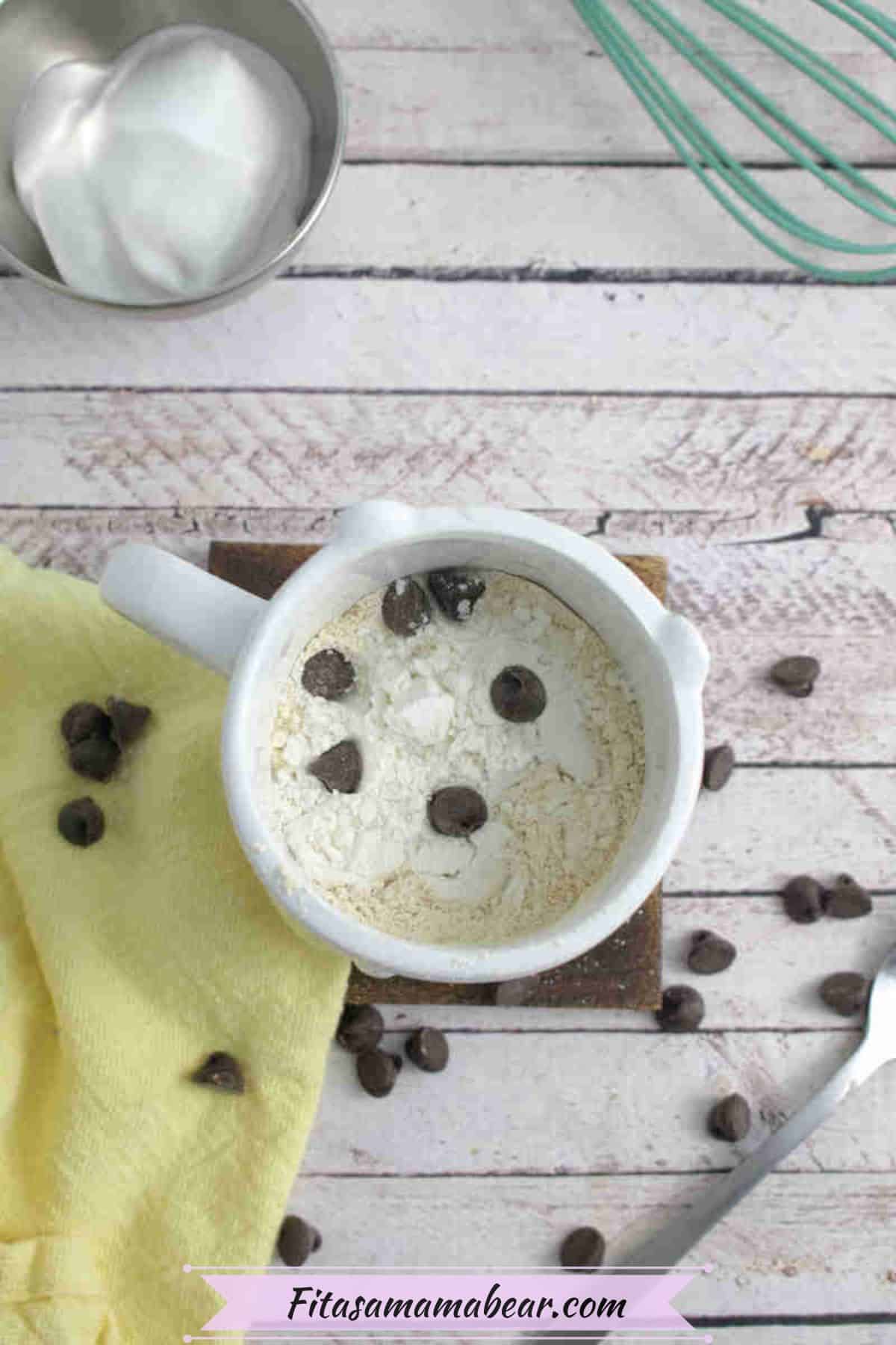 White mug with protein powder and flour in it and chocolate chips in and around it with a yellow linen beside it.