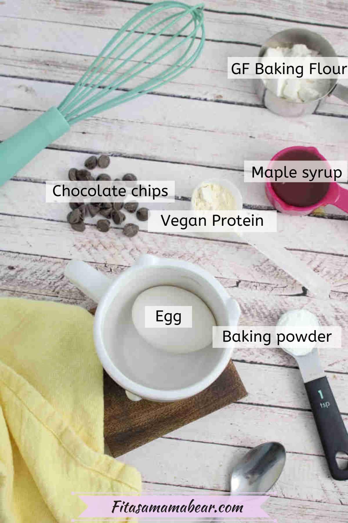 Multiple ingredients to make a chocolate chip protein mug cake in measuring cups with text labels over them.