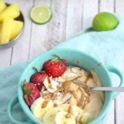 Papaya smoothie bowl topped with berries, banana and coconut in a blue bowl with a spoon and fresh fruit behind it.