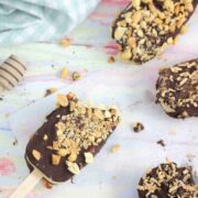 Chocolate coated ice cream bars with peanuts on parchment paper with one having a bite out of it.