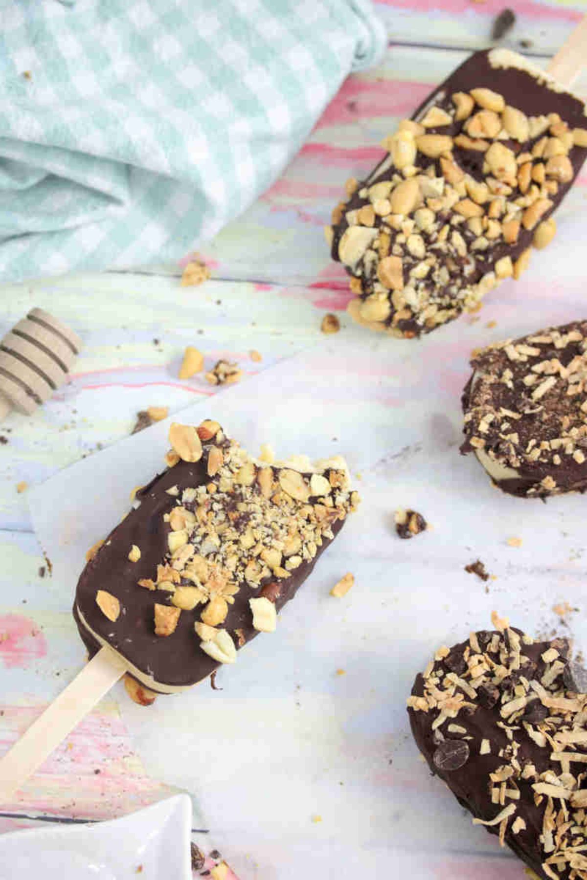 Chocolate coated ice cream bars with peanuts on parchment paper with one having a bite out of it.