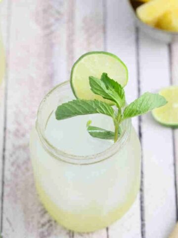 Ginger beer mocktail in a mason jar with fresh mint and lime on the jar and ingredients and another jar around it.