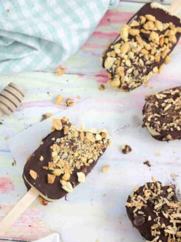 Chocolate coated ice cream bars with peanuts on parchment paper with one having a bite out of it.