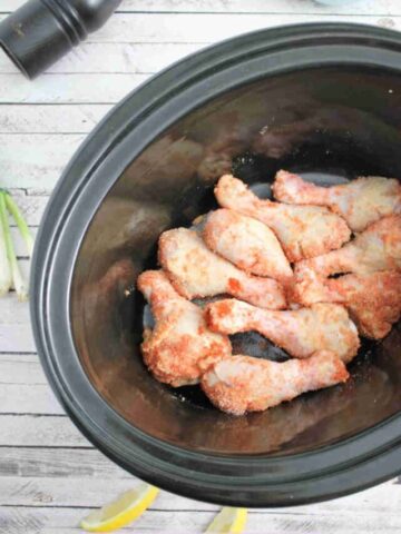 Raw chicken legs seasoned with spices in a black slow cooker.
