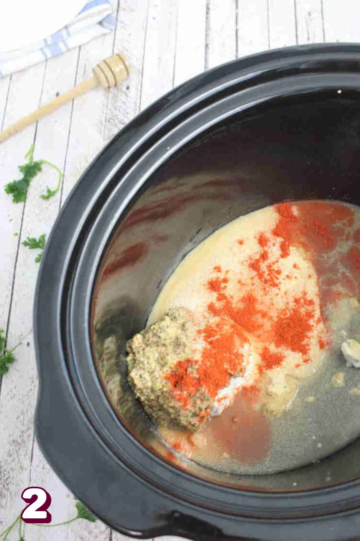 Black slow cooker with ingredients to make a honey mustard sauce in it and parsley around it.