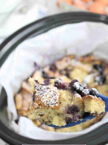 Close up of spoon over a slow cooker lined with parchment paper and filled with high protein French toast casserole with blueberries