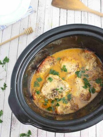 Black slow cooker with honey mustard chicken thighs topped with parsley on top.