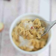 Apple mug cake in a white ramekin with coconut milk on top and spoon pilling out of it.