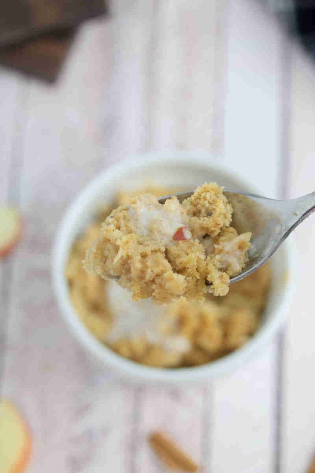 Apple mug cake in a white ramekin with coconut milk on top and spoon pilling out of it.