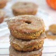 Three gluten-free pumpkin donuts stacked on top of one another with more donuts in the background.