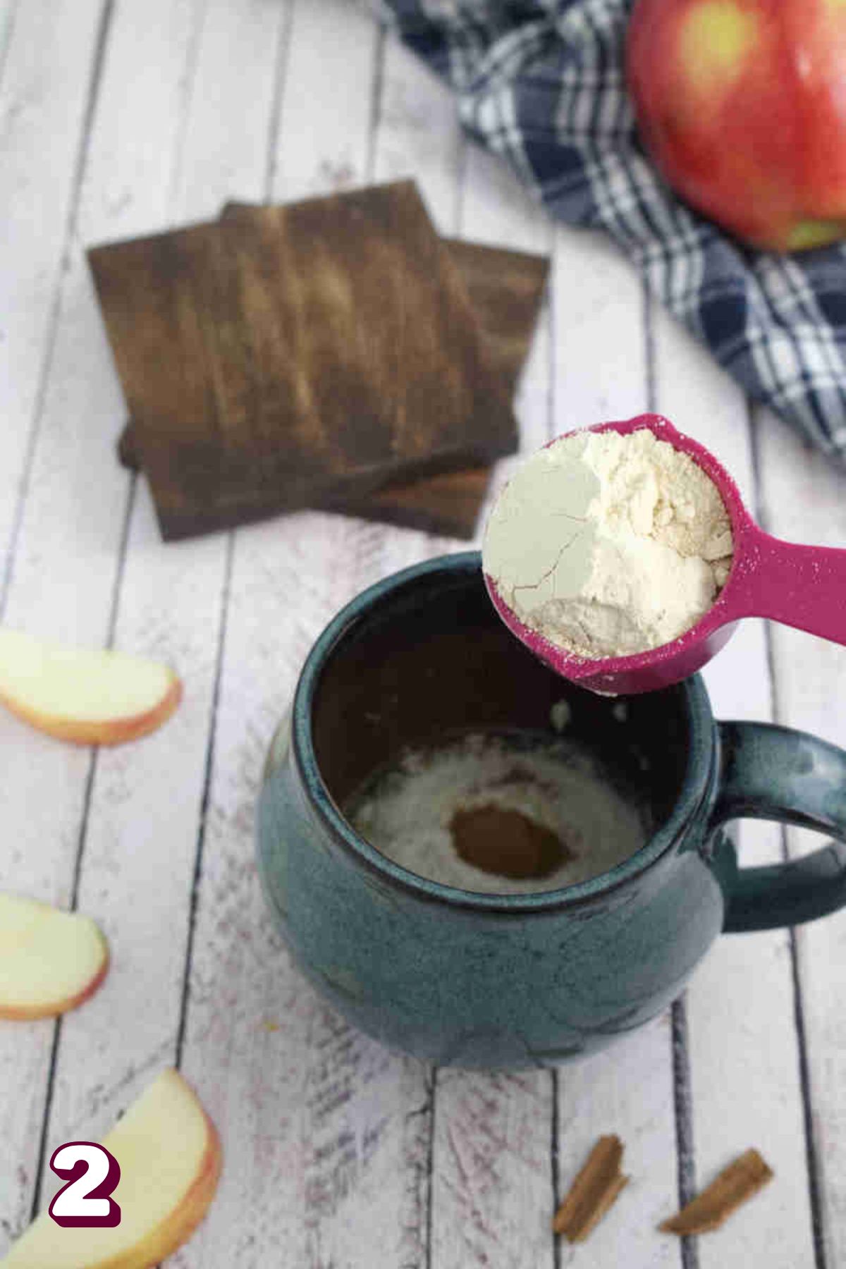 Protein powder being added to a blue mug with flour in it and apples around it.