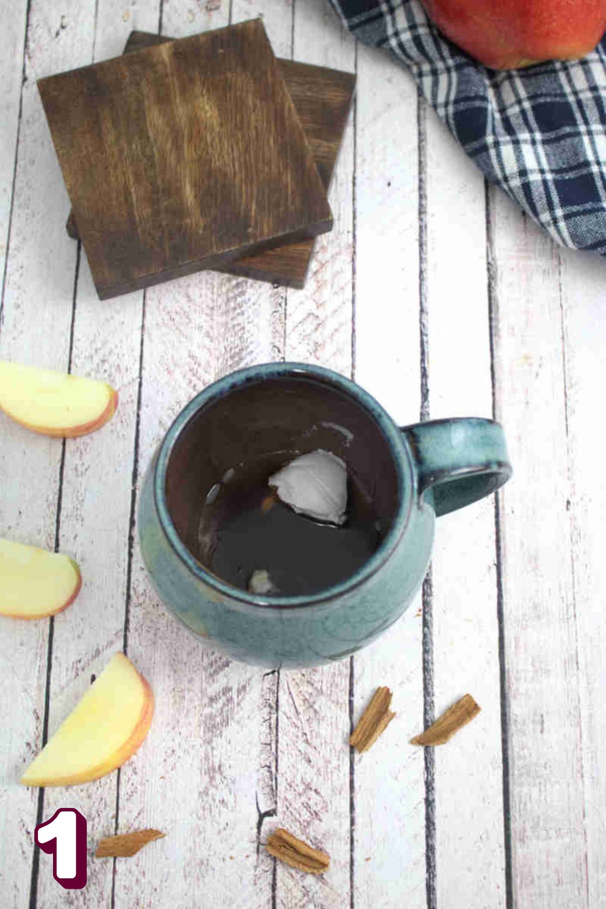 Blue mug with maple syrup, coconut milk in it and apples around it.