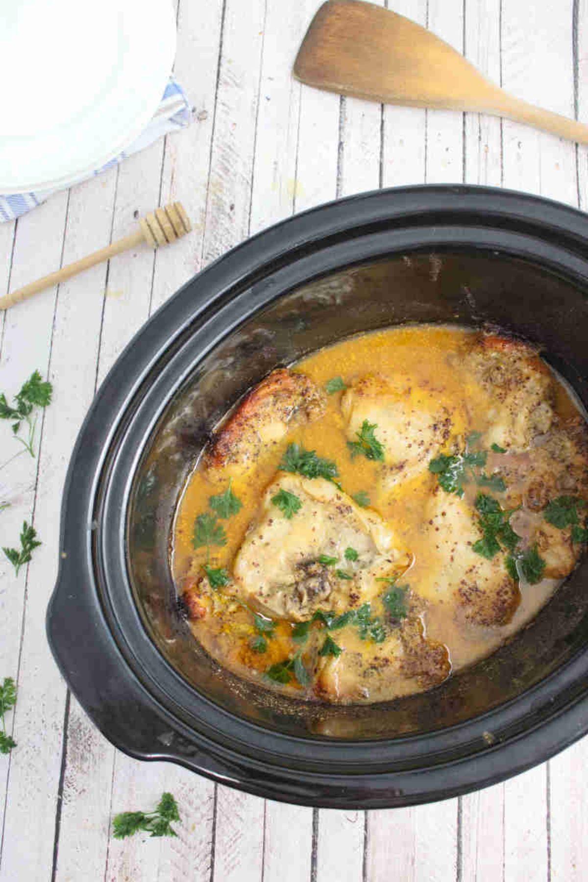 Black slow cooker with honey mustard chicken thighs topped with parsley on top.