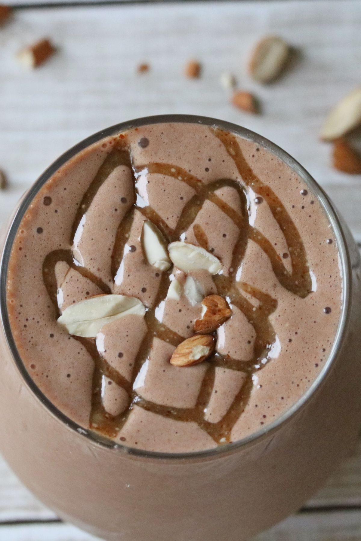 Chunky monkey protein shake with caramel drizzled on top and chopped almonds on the shake and around it.