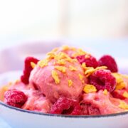 Close up of raspberry protein frozen yogurt in a white bowl topped with cereal and a light linen behind it.