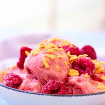 Close up of raspberry protein frozen yogurt in a white bowl topped with cereal and a light linen behind it.