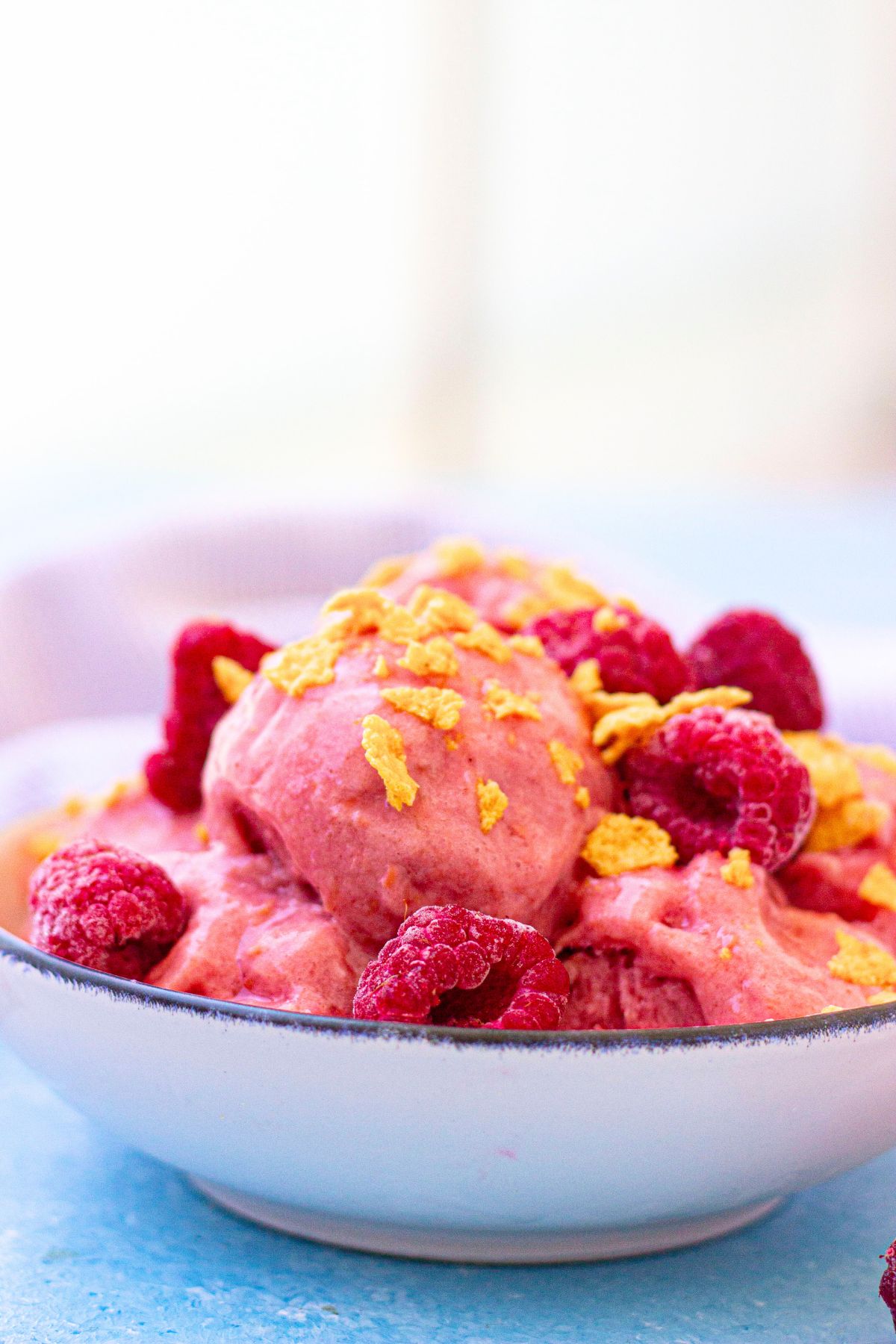 Close up of raspberry protein frozen yogurt in a white bowl topped with cereal and a light linen behind it.