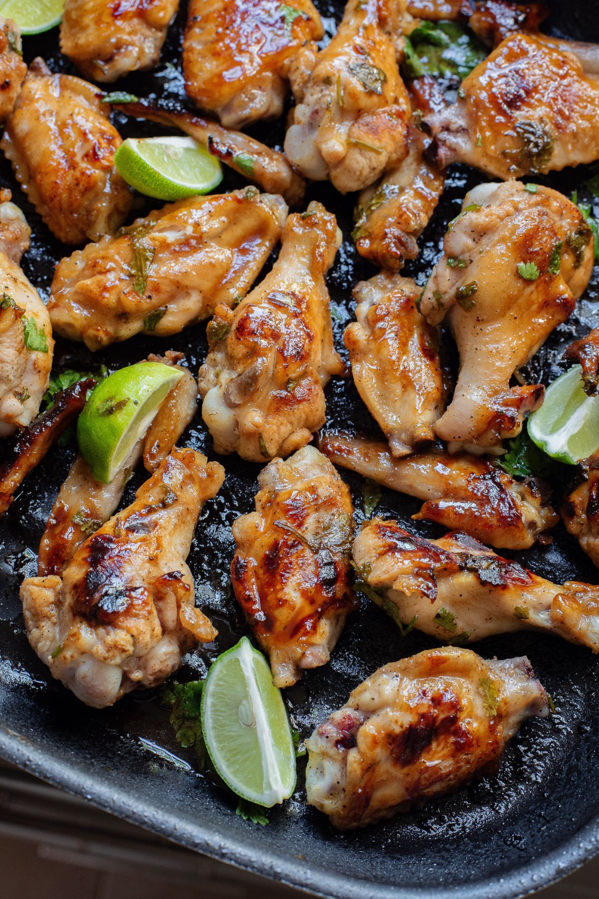 Gluten-free chicken wings in honey garlic sauce on a grill pan with cilantro and lime on them.