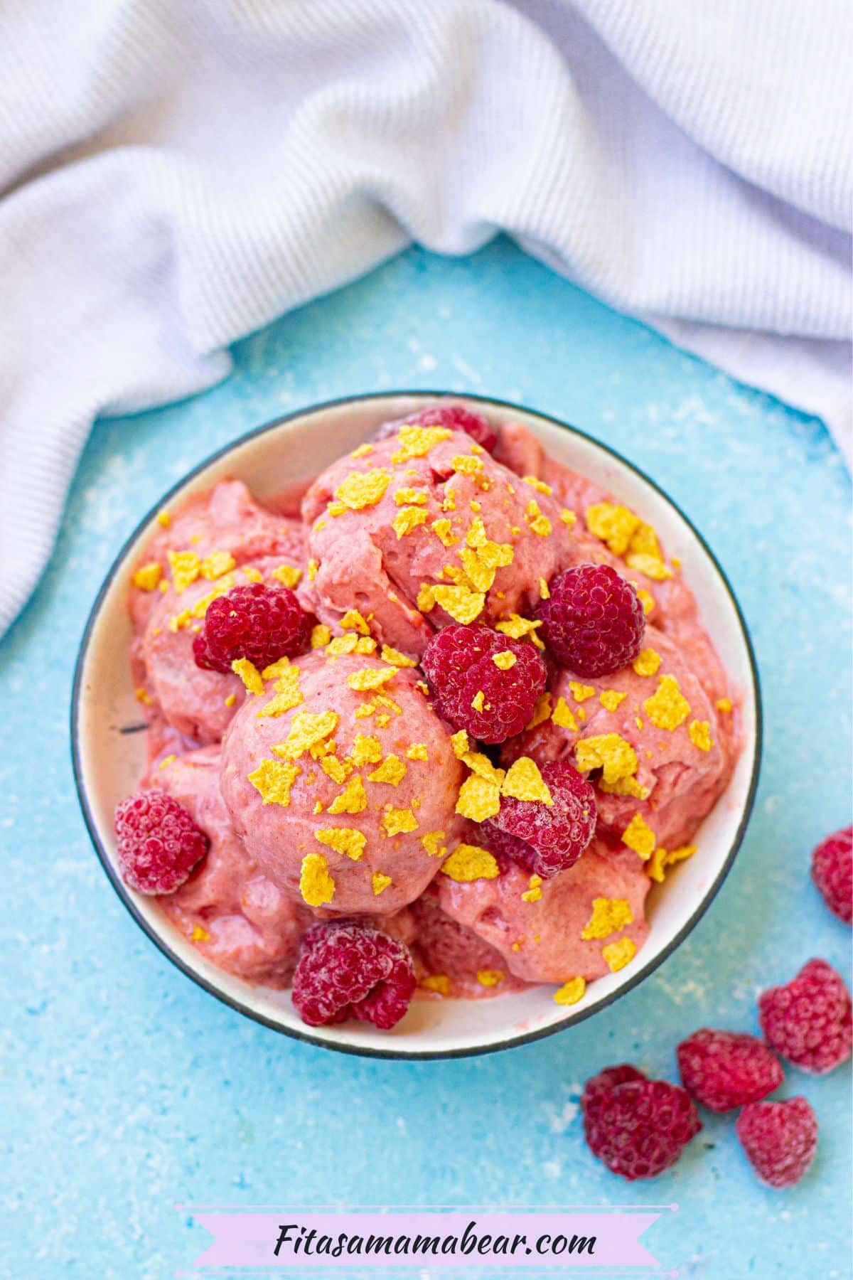 Raspberr protein frozen yogurt in a white bowl topped with cereal and a light linen behind it.