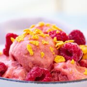Close up of raspberry protein frozen yogurt in a white bowl topped with cereal and a light linen behind it.