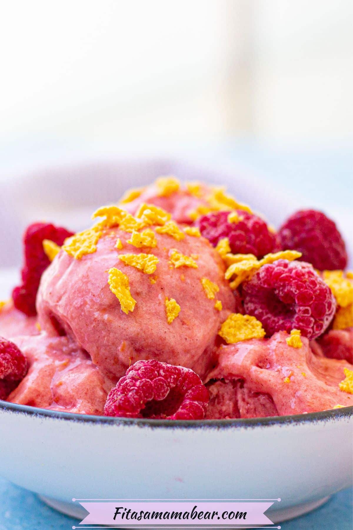 Close up of raspberry protein frozen yogurt in a white bowl topped with cereal and a light linen behind it.