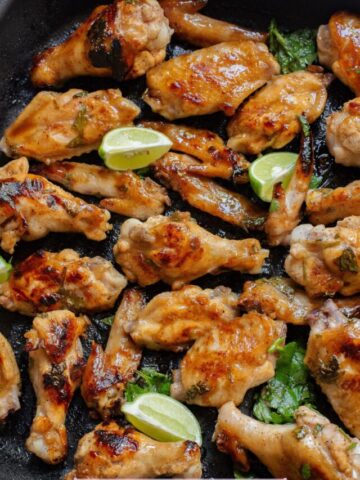 Gluten-free chicken wings in honey garlic sauce on a grill pan with cilantro and lime on them