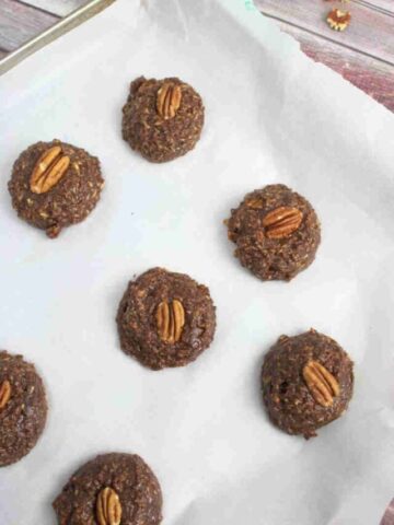 Raw chocolate pregnancy cookies topped with pecans on a baking sheet lined with parchment paper.