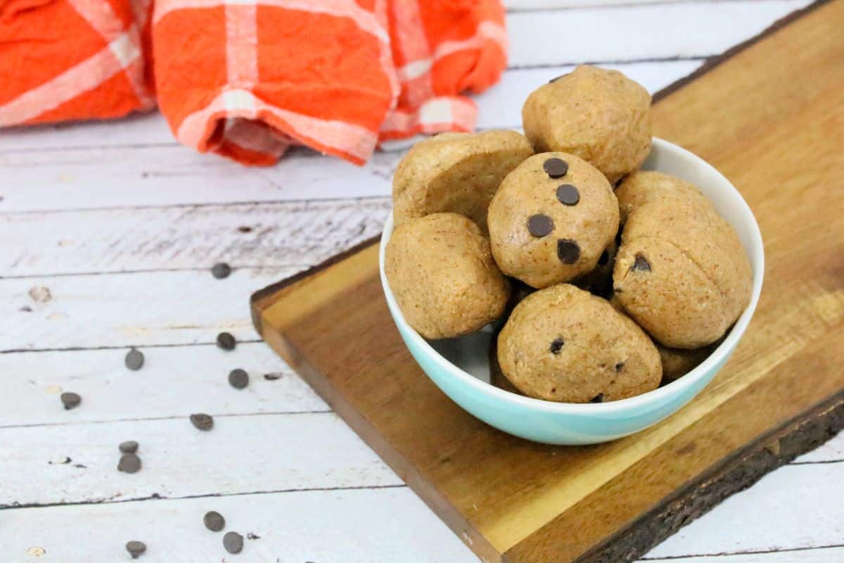 Paleo cookie dough ball being held between fingers with more in a bowl.