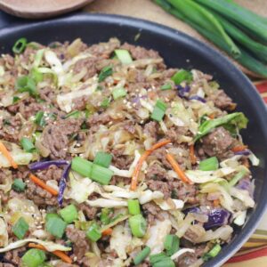 Inside out egg roll in a skillet with green onions on top and a wooden spoon and white plates behind it.
