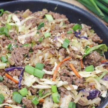 Inside out egg roll in a skillet with green onions on top and a wooden spoon and white plates behind it.