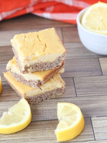 Three paleo lemon bars stacked with cut lemons around it and more behind them.