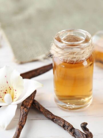 White flower on vanilla beans with extract in a glass jar beside it.