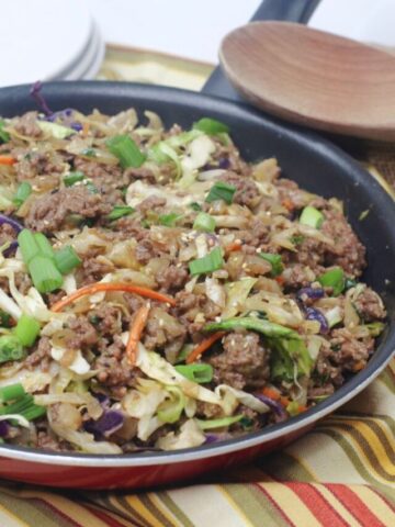 Inside out egg roll in a skillet with green onions on top and a wooden spoon and white plates behind it.