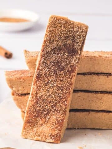 Snickerdoodle protein bars stacked with one bar in front and cinnamon sticks and milk behind it.