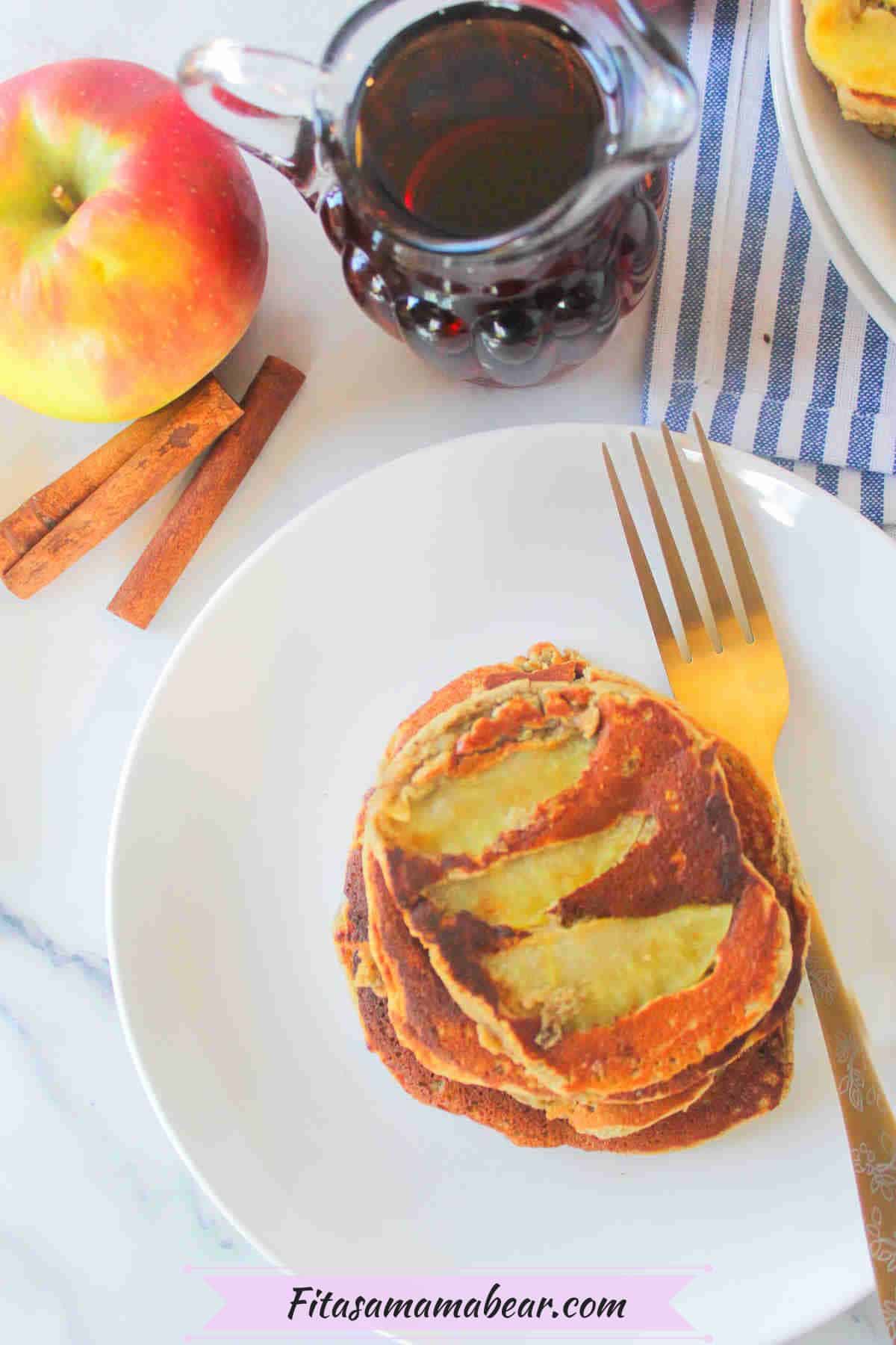 Apple cinnamon pancakes stacked on a white plate with a fork on it.