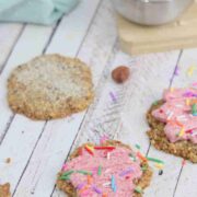 Sugar cookies with pink icing and sprinkles, a blue linen and bowl of sugar behind them.