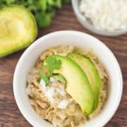 White ramekin topped with shredded chicken, onion and avocados on a cutting board.