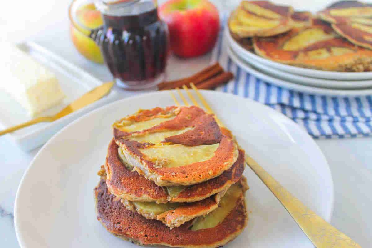 Apple protein pancakes stacked on a white plate with a fork on it.