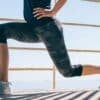 Lower half of a woman in tights and a tank top in a lunge position.