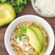 White ramekin topped with shredded chicken, onion and avocados on a cutting board.