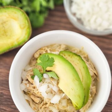 White ramekin topped with shredded chicken, onion and avocados on a cutting board.