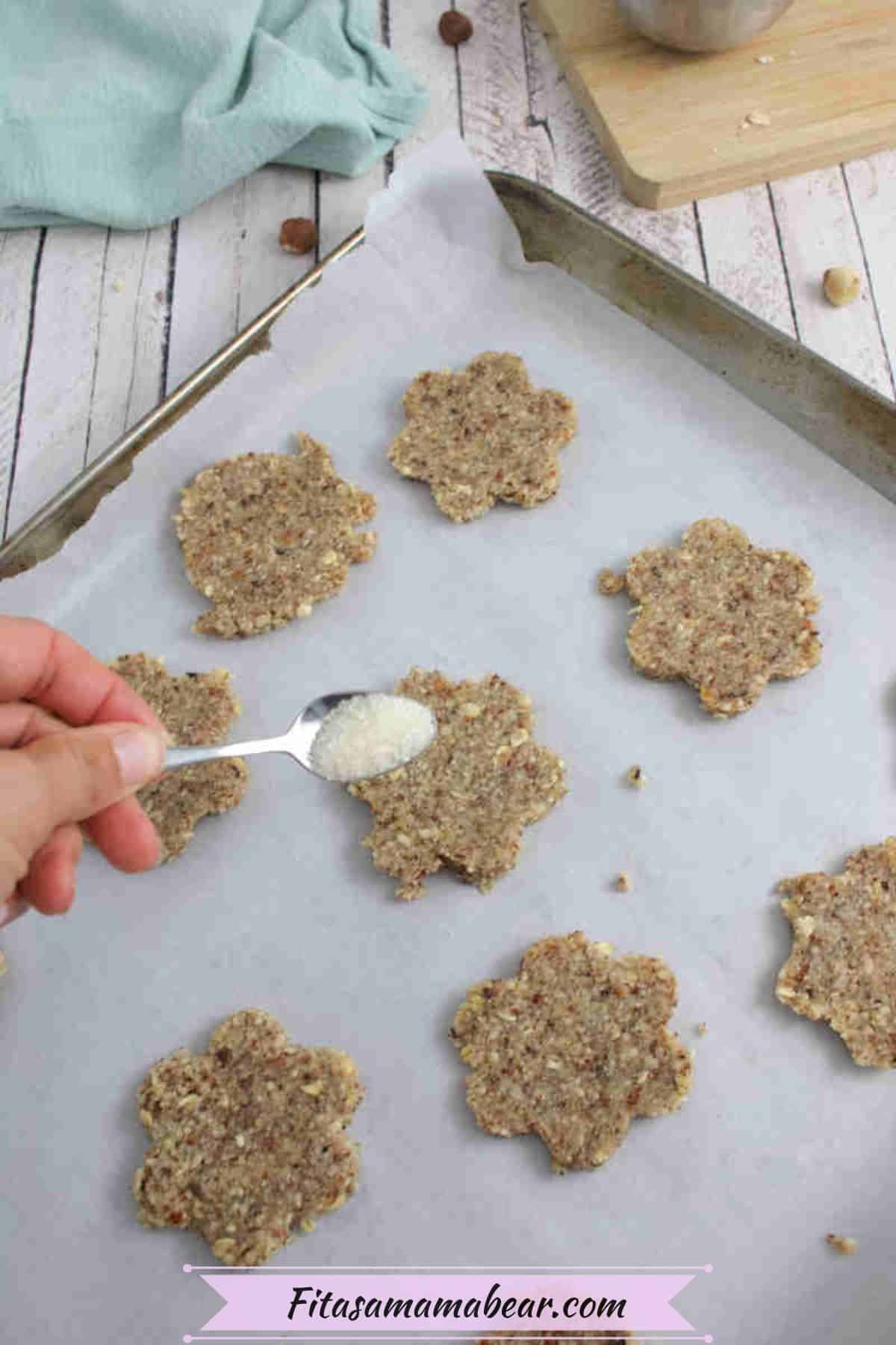 Sugar being sprinkled on raw cookies on a baking tray.