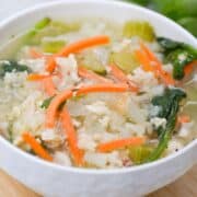 Chicken and cauliflower rice soup with carrots in a white bowl on a wooden cutting board.