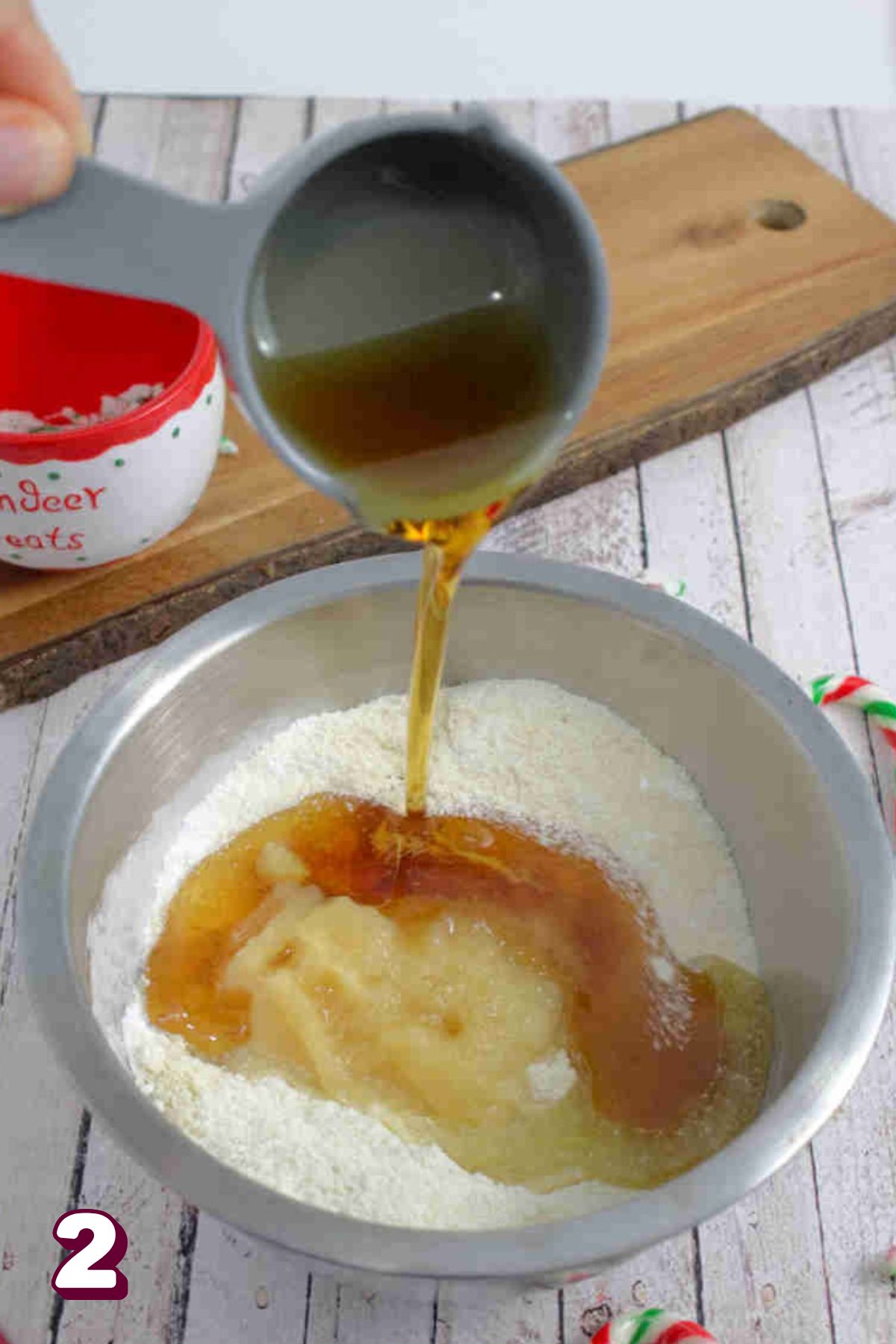 Maple syrup being poured into a steel bowl with almond and coconut flour.