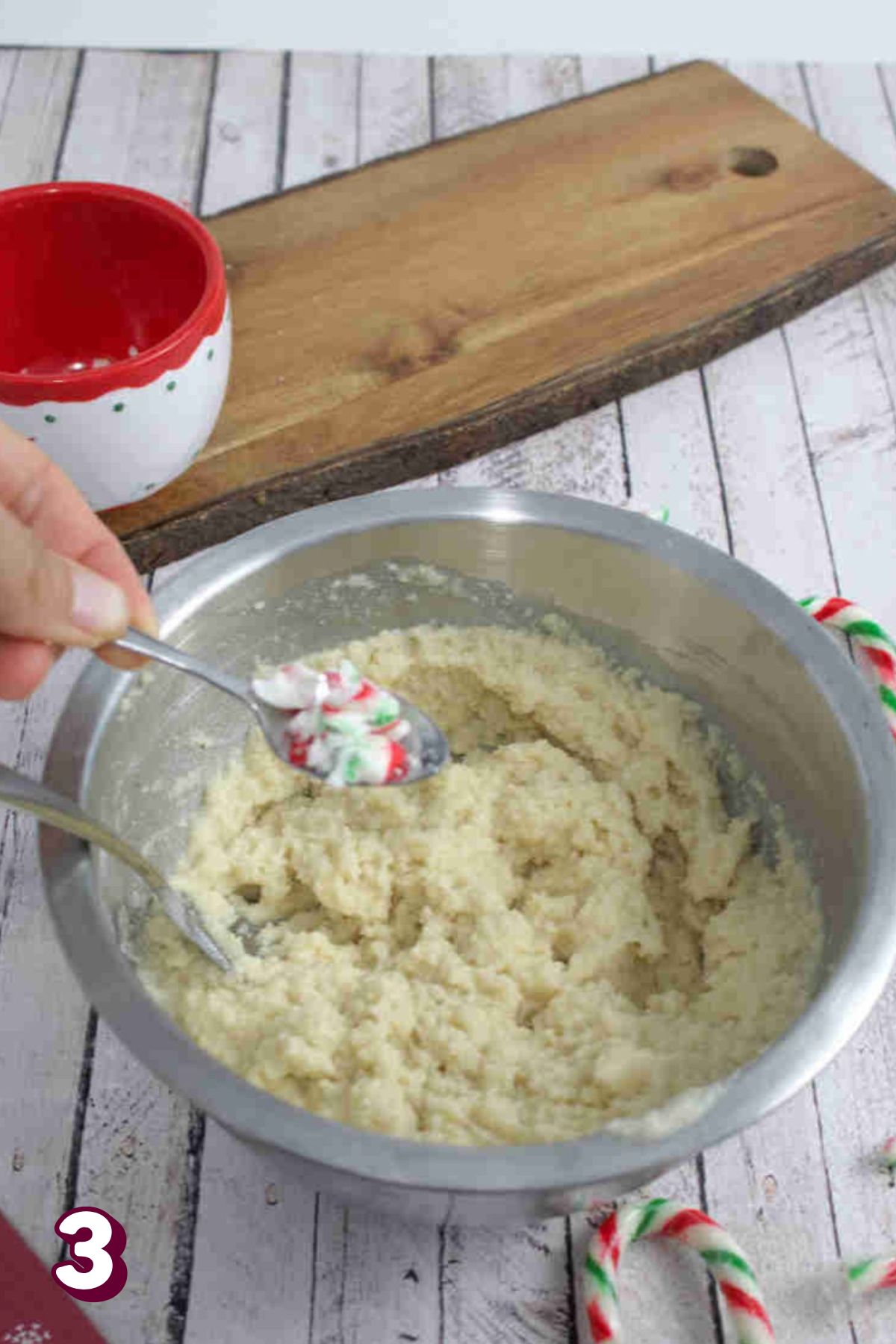 Candy canes being added to raw donut batter in a steel bowl.