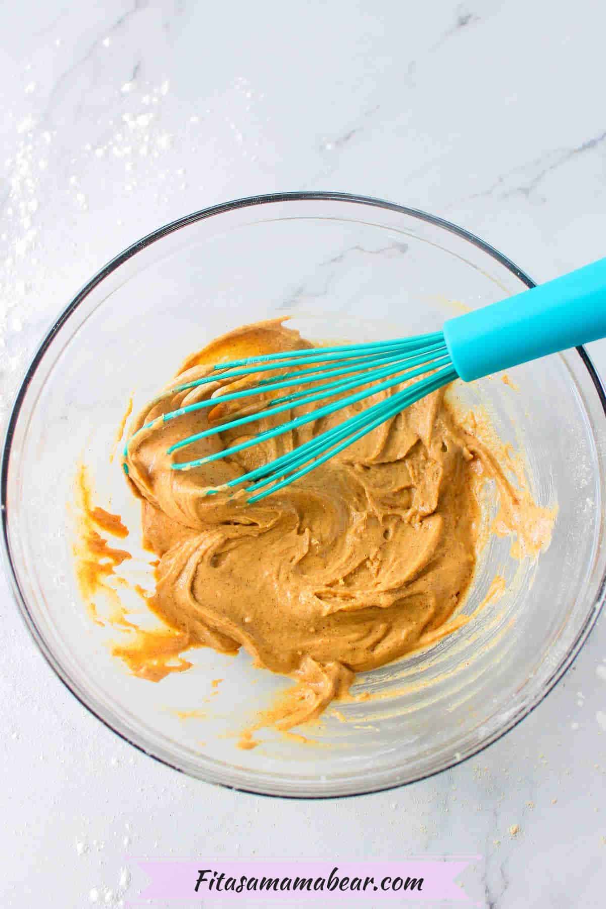 Raw protein pancake batter in a glass bowl with a blue whisk.